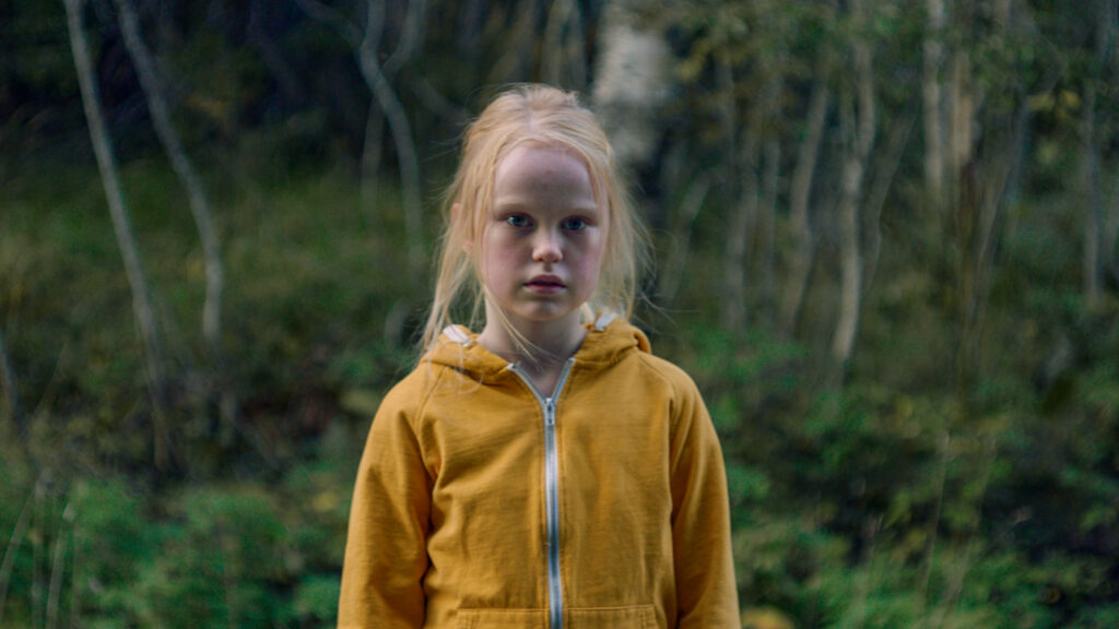Hauptfigur Ida steht mit einer gelben Jacke vor dem Waldrand in The Innocents