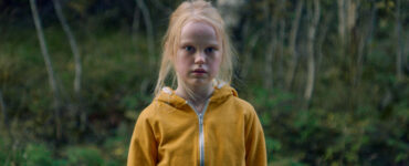 Hauptfigur Ida steht mit einer gelben Jacke vor dem Waldrand in The Innocents