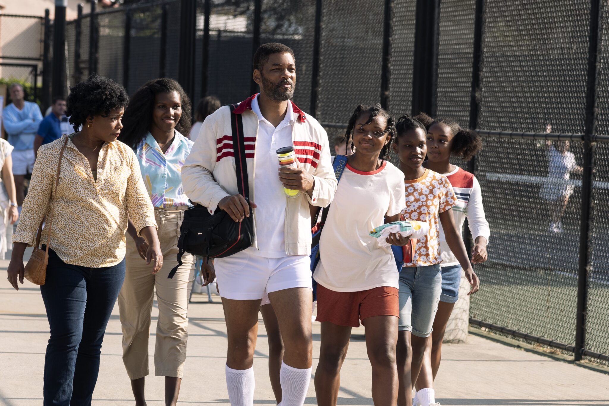 Ein Bild aus dem Film King Richard, Will Smith und die anderen afro-amerikanischen Darstellerinnen sind in einer Tennisanlage zu sehen. 