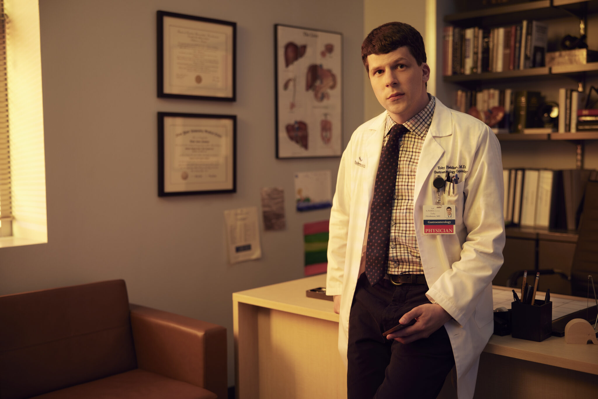 Jesse Eisenberg als Arzt an seinem Schreibtisch stehend.