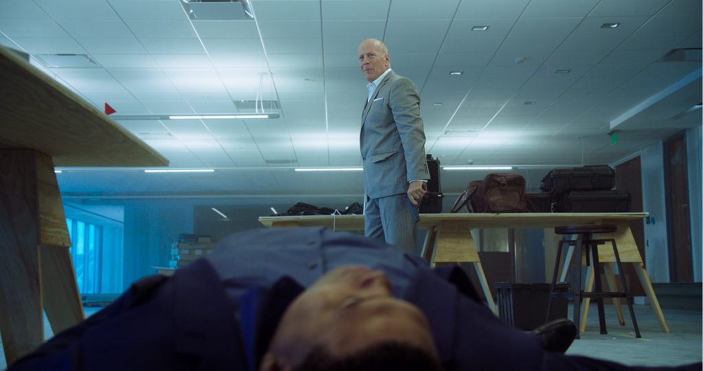 Bruce Willis steht als Rex mit der Waffe in der Hand vor einem auf dem Boden liegenden, toten Kompagnon in 10 Minutes Gone