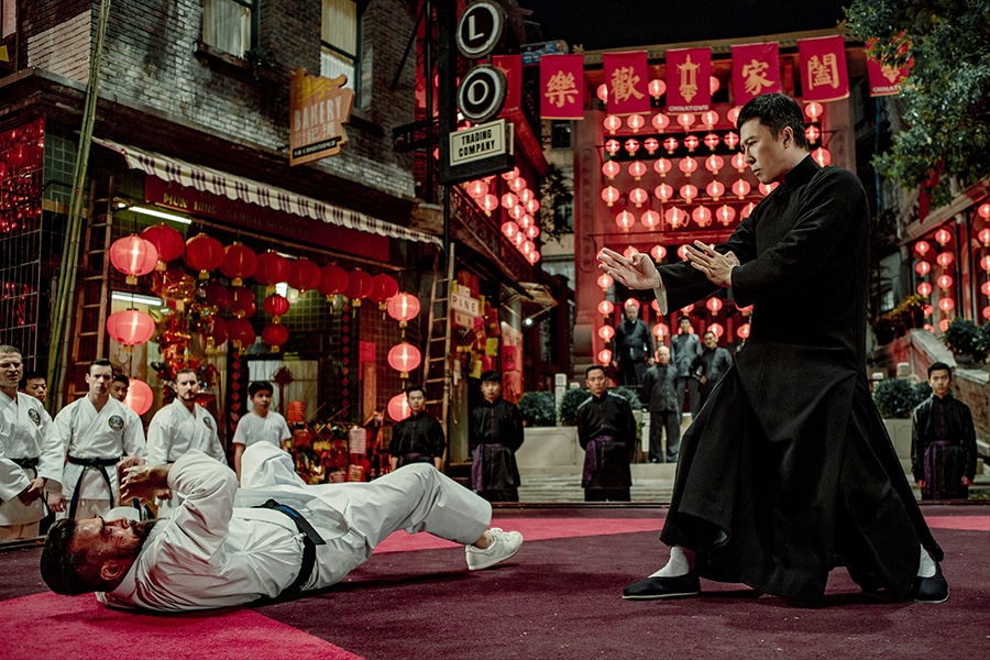 Der in Schwarz gekleidete Ip Man (Donnie Yen) befindet sich in einem Duell mit einem weiß gekleideten Kontrahenten, der auf den Boden geworfen wurde. Im Hintergrund sieht man einige weitere Kampfkunst-Schüler auf dem Boden knien. Die etlichen roten Lampions sorgen für eine wunderschöne Kulisse. 