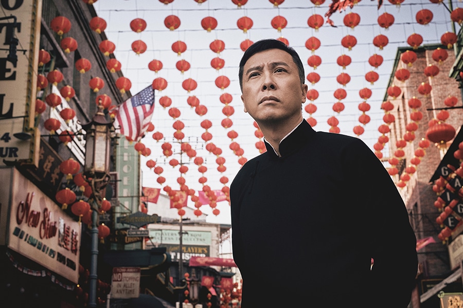 Ip Man (Donnie Yen) steht mit nachdenklicher Miene und aufrechter Haltung in Chinatown in San Francisco. Hinter ihm sind dutzende rote, klassisch chinesische Lampions zu sehen, außerdem eine an der Häuserfassade angebrachte amerikanische Flagge.