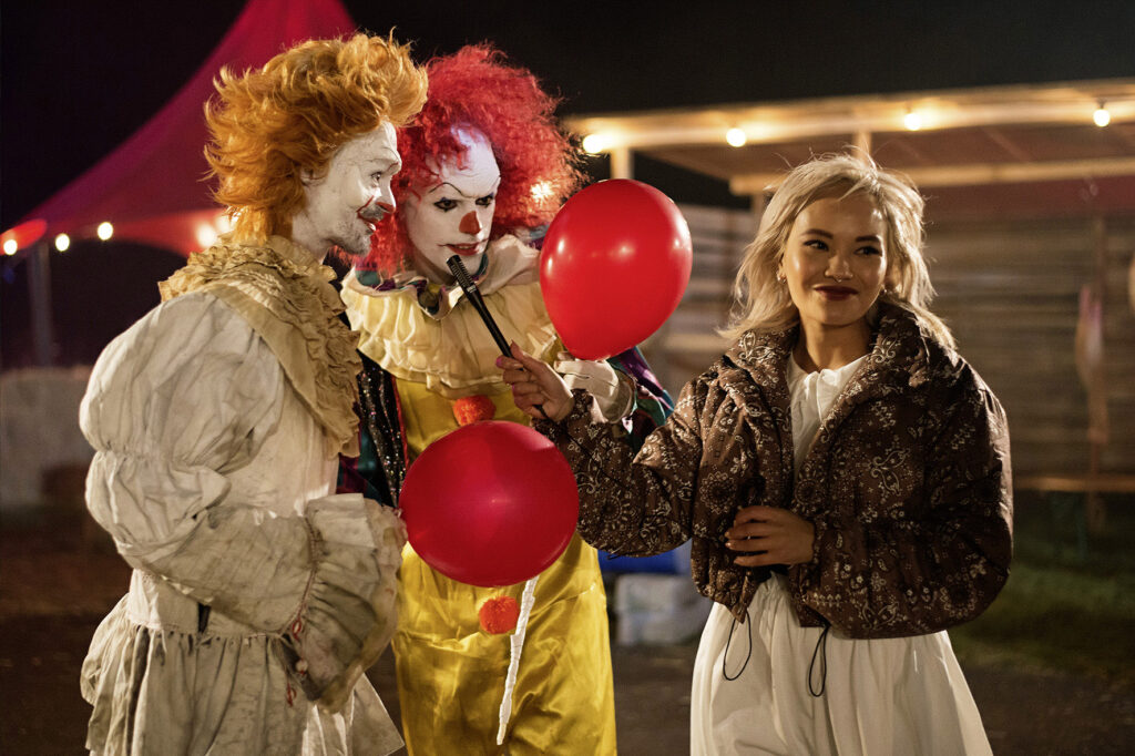 Eine blonde Festivalbesucherin steht neben zwei gruseligen Clowns, die sie angucken.