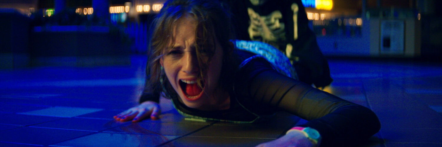 Maya Hawke als Heather in Fear Street Teil 1. Sie liegt schreiend auf dem Boden und wird von hinten am Bein gehalten