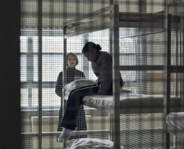 Brooklyn Letexier-Hart sitzt mit gesenktem Kopf im Etagenbett ihrer Zelle, die einem Käfig ähnelt - Night Raiders