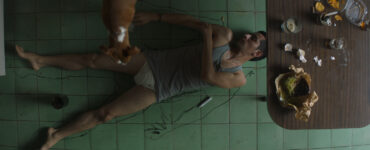 Montoya liegt auf dem Küchenboden und zeichnet seinen Körperumriss auf den Boden, während sein Hund zusieht - A Cop Movie