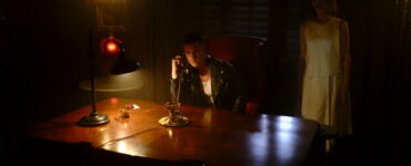 Zack (Mike Manning) sitzt in einem knapp beleuchteten Raum und hat den Telefonhörer in der Hand, während hinter ihm die verstorbene Edith (Lin Shaye) steht.