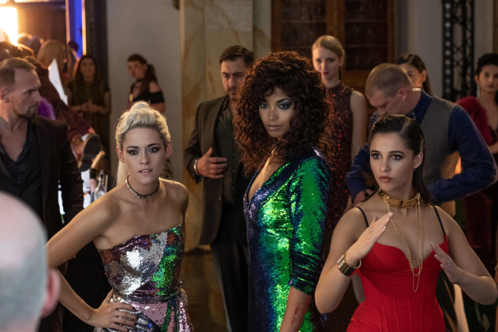 Kristen Stewart als Sabina, Ella Balinska als Jane und Naomi Scott als Elena stehen kampfbereit in eleganten Kleidern in einer Menschenmenge während einer Gala im 2019er "3 Engel Für Charlie".