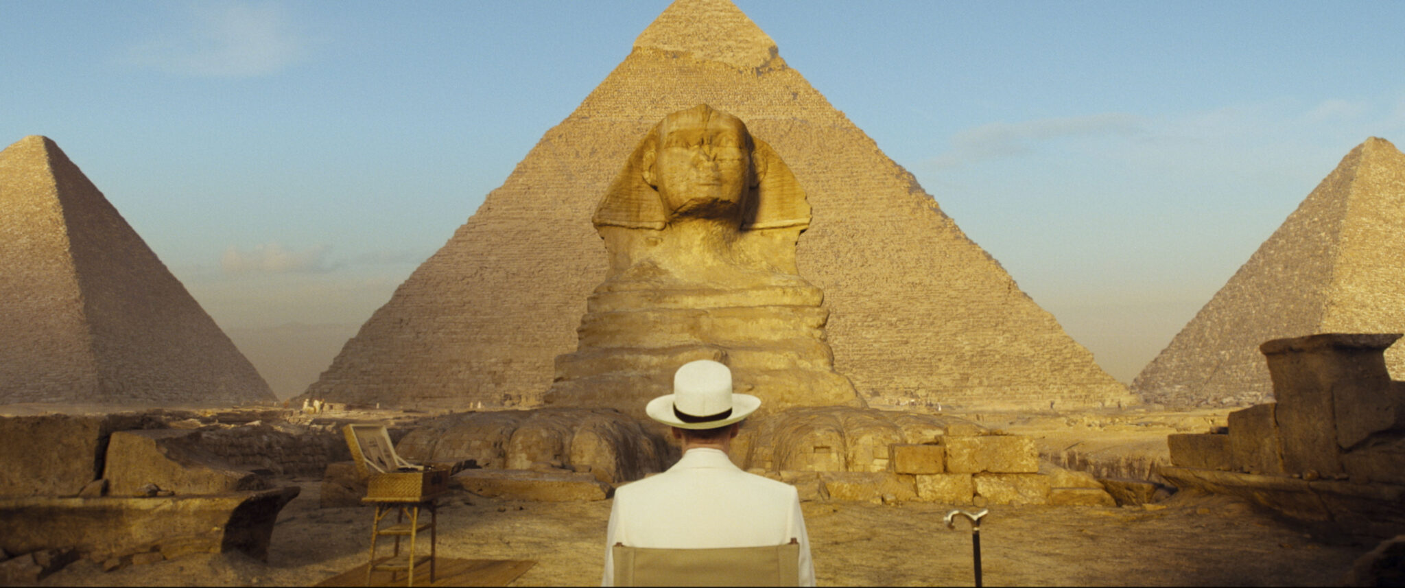 Kenneth Branagh sitzt abgewandt auf einem Stuhl. Er sieht in die Ferne und betrachtet die Pyramiden, die den Großteil des Bilds ausmachen - Tod auf dem Nil