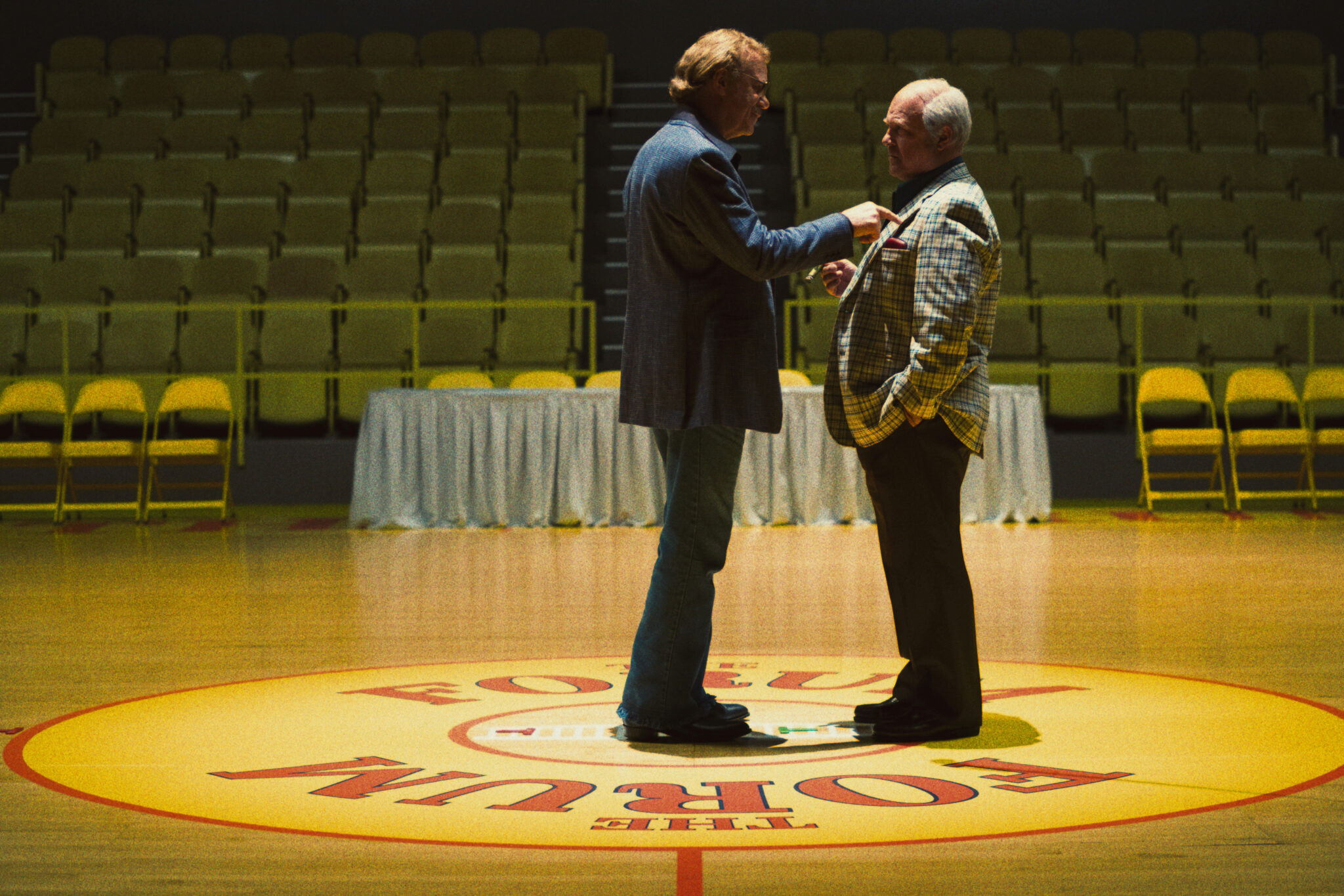 John C. Reilly als Jerry Buss in der Mitte eines Basketballspielfelds. Er bedroht einen zweiten Mann im Anzug, der vor ihm steht. Winning Time