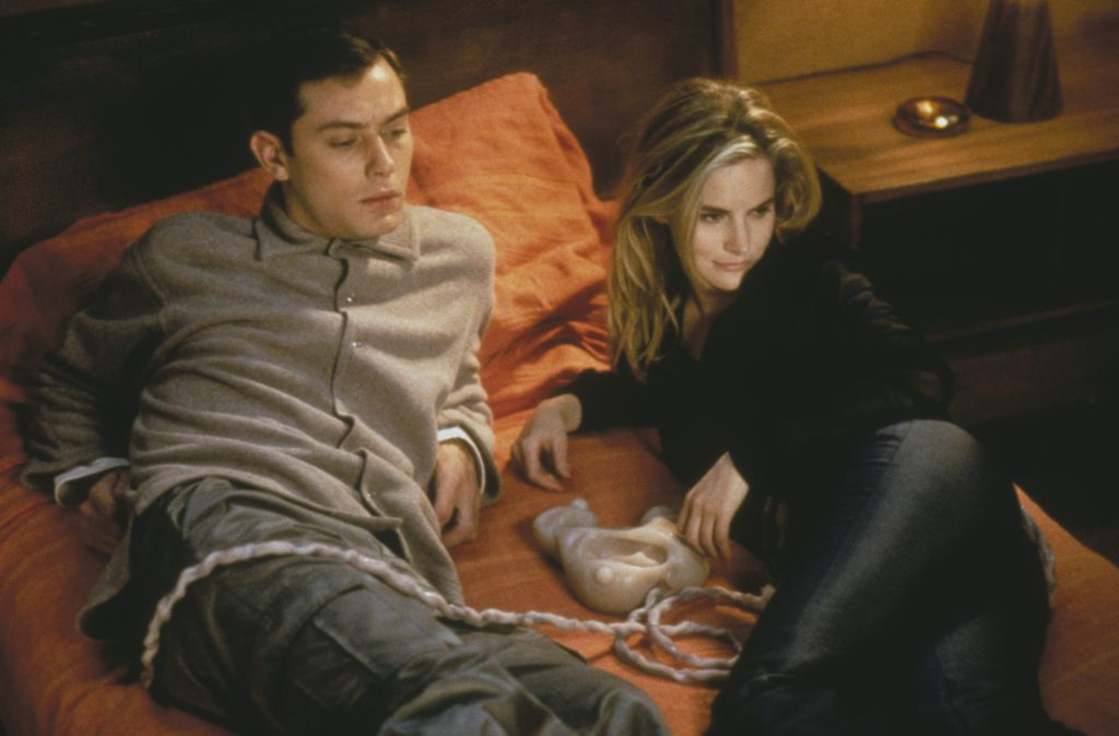 Jennifer Jason Leigh und Jude Law haben es sich auf dem Bett gemütlich gemacht und die organische Konsole eingestöpselt, um eXistenZ zu spielen