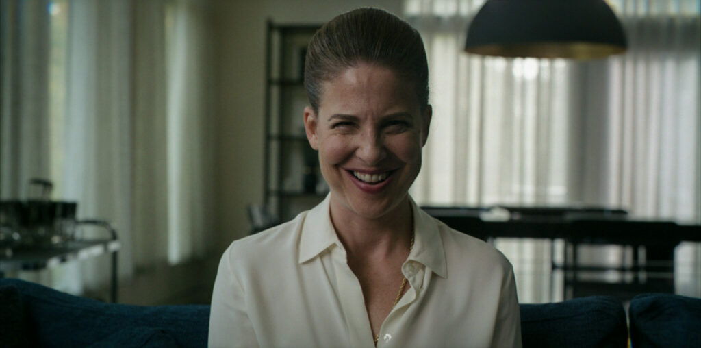 Eine Frau mit grässlichem Lachen, weißer Bluse. Sie guckt in die Kamera. Es ist die Schauspielerin Robin Weigert im Film Smile - Siehst du es auch?
