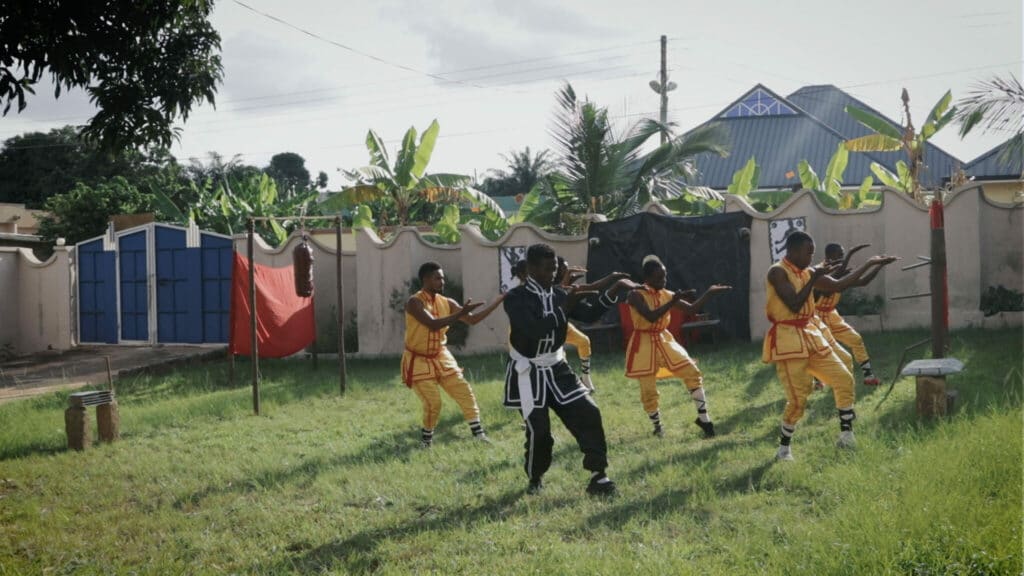 Der Übungsleiter in schwarzer Tracht zeigt seinen Schülern in gelber Tracht die richtigen Moves in African Kung-Fu Nazis