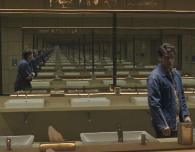 Stephen Grant steht in einem Waschraum zwischen Spiegeln, die sich endlos weiter reflektieren.