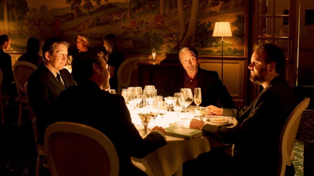 Martin, Tommy, Peter und Nikolaj sitzen gemeinsam an einem Tisch im Restaurant und unterhalten sich, während Sekt und Bier auf dem Tisch steht. Another Round ist der Abschlussfilm des Film Fstival Cologne 2020