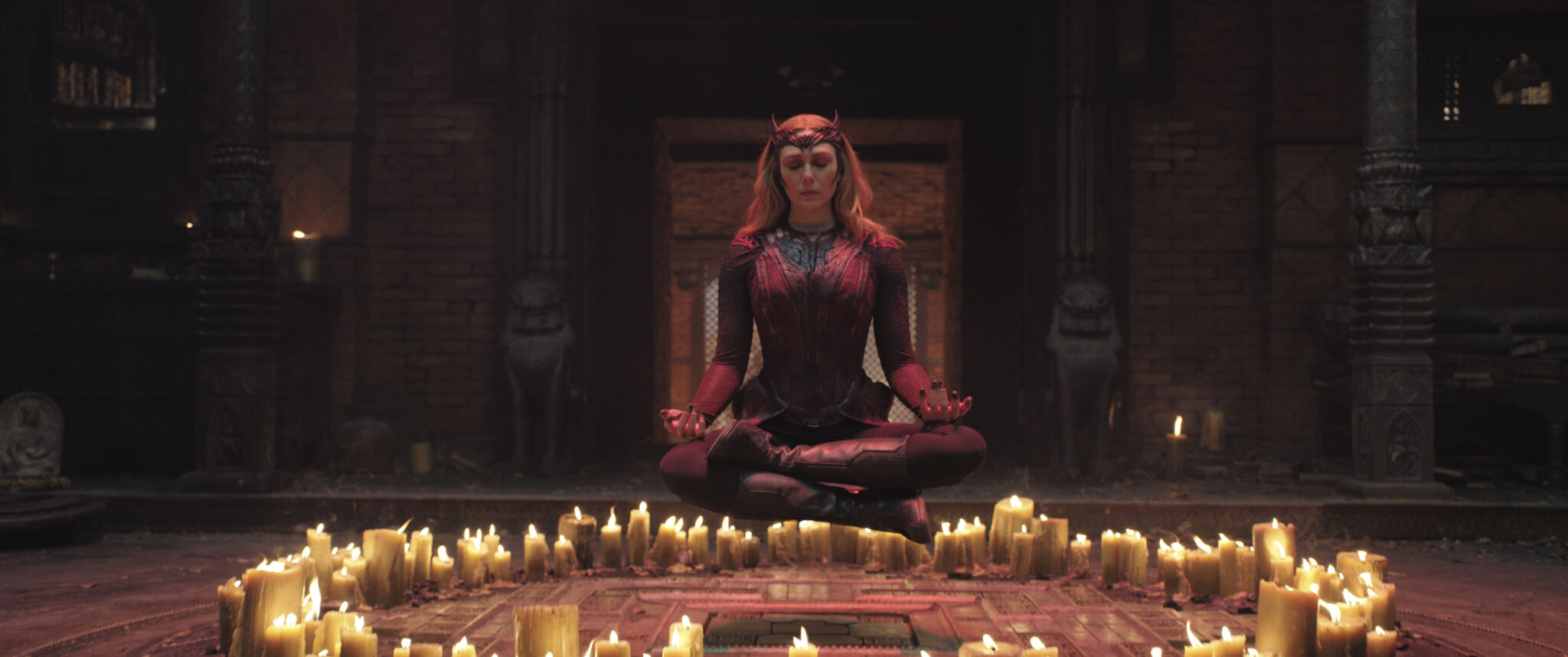 Elizabeth Olsen schwebt als Hexe in rotem Gewand über einem Kreis aus Kerzen und sitzt dabei im Schneidersitz. Doctor Strange in The Multiverse of Madness