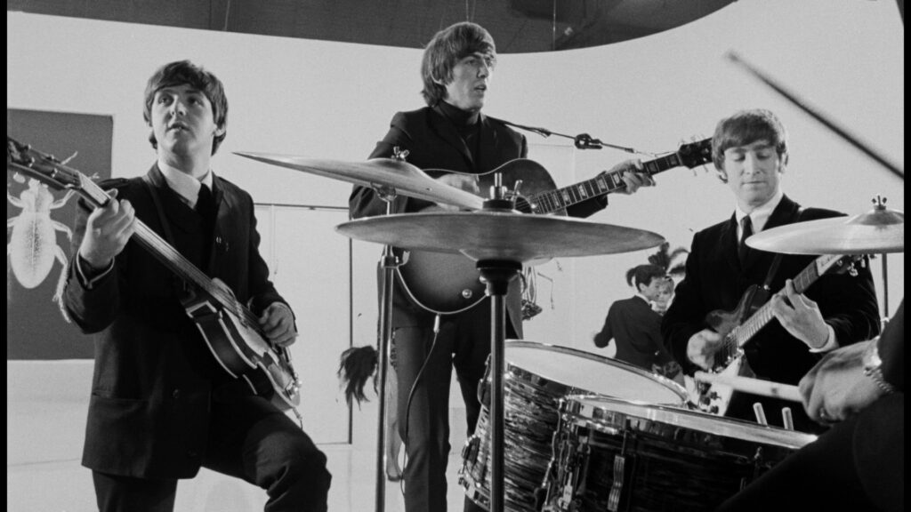 Vor einem weißen Bildhintergrund spielt die Musikgruppe The Beatles im Film A Hard Day's Night.