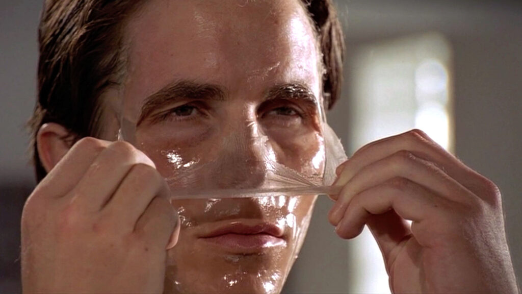 Christian Bale zieht sich als Patrick Bateman eine Schönheitsmaske vom Gesicht.