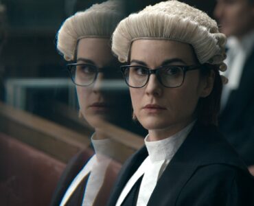 Michelle Dockery in Richterrobe mit weißer Perücke vor weiteren Gerichtsbeamten mit ernster Miene.
