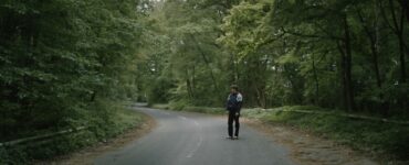 Erik steht alleine auf einer Straße die durch einen Wald führt - Arboretum
