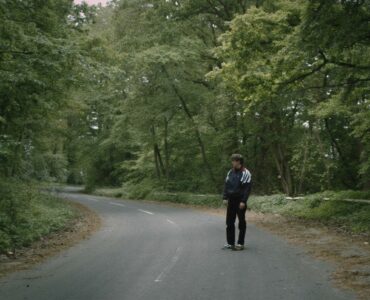 Erik steht alleine auf einer Straße die durch einen Wald führt - Arboretum