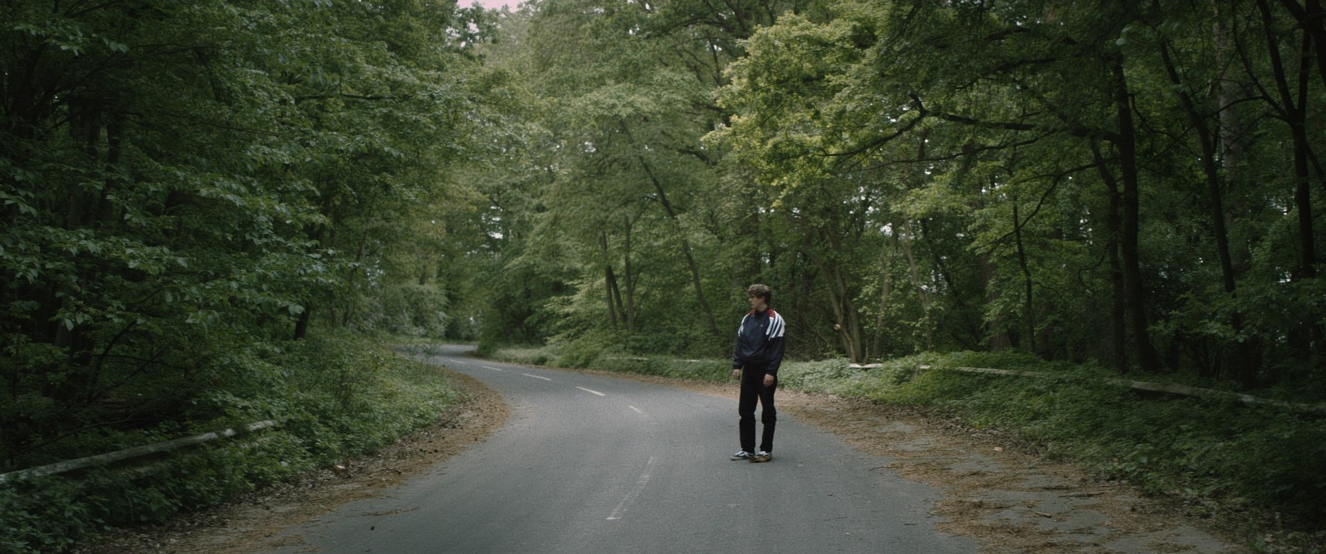 Erik steht alleine auf einer Straße die durch einen Wald führt