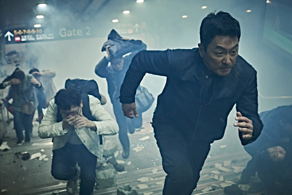 Hauptfigur In-chang Jo (gespielt von Ha Jung-woo) versucht sich inmitten eines Erdbebens in Sicherheit zu bringen indem er rennt. Es ist kaum was zu erkennen, da sehr viel staub in der Luft ist. Es sind weitere Menschen im Hintergrund zu erkennen, die versuchen in Deckung zu gehen oder um ihr Leben zu rennen.