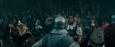 Arminius schaut mitten im Schlachtgetümmel von Barbaren überrascht und angestrengt, mit rot-schwarzer Kriegsbemalung im Gesicht. Um ihn herum bekämpfen sich etliche Krieger.