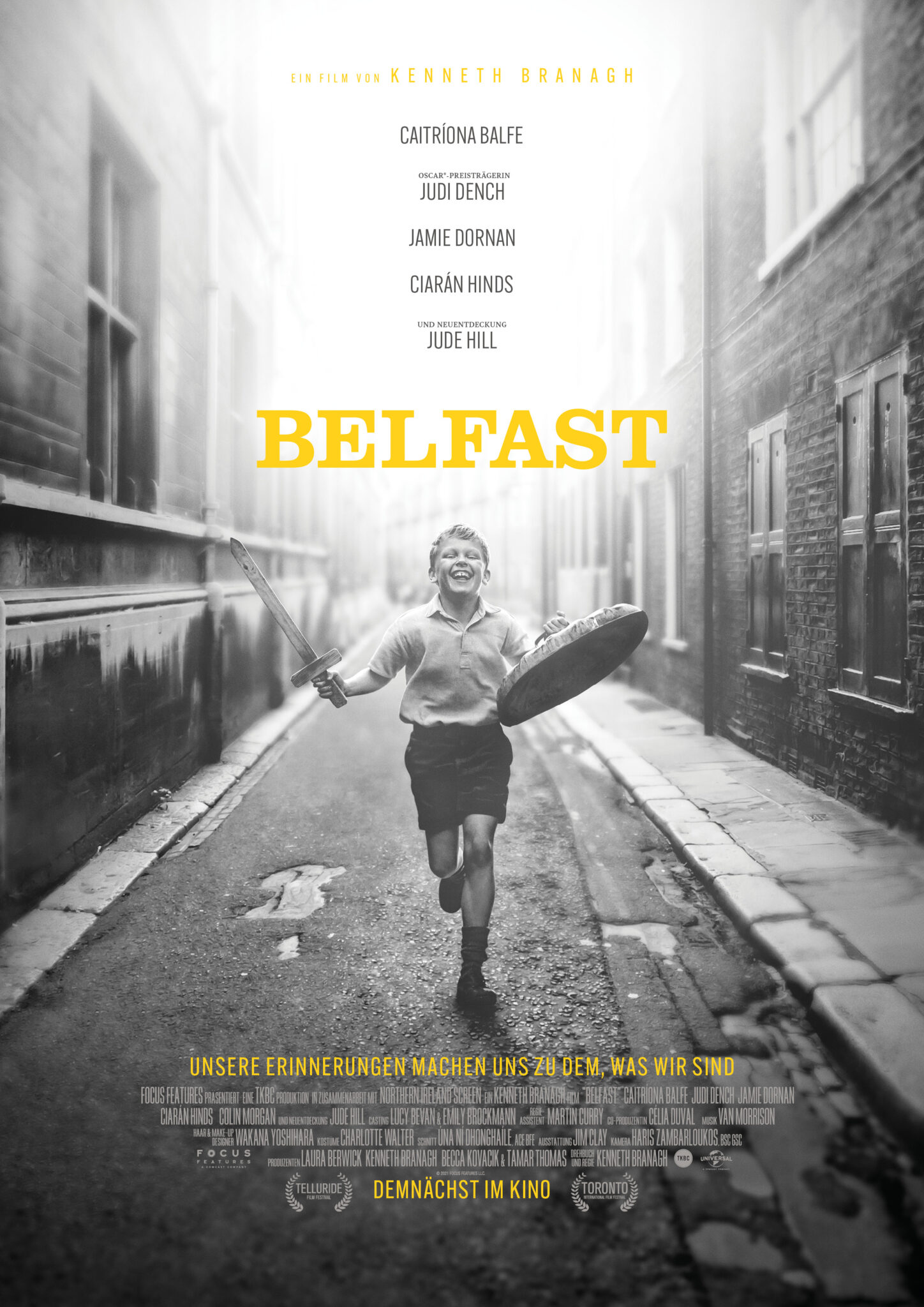 Im Hauptplakat von Belfast läuft ein kleiner Junge mit Holzschwert und Schild durch eine schwarz-weiße Straße -Belfast