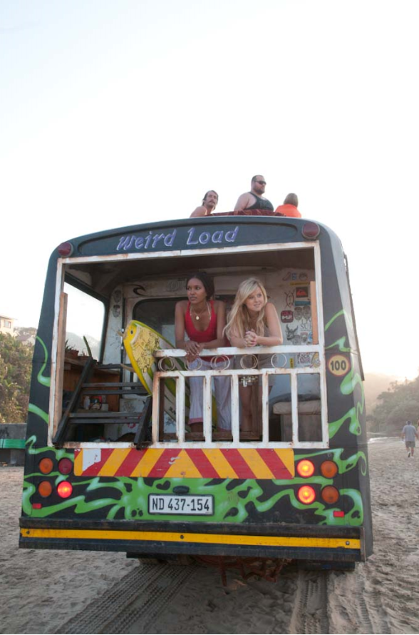 Elizabeth Mathis als Pushy und Sasha Jackson als Dana lehnen sich ans Geländer an der Hinterseite eines bunten Hippiebusses und betrachten die afrikanische Landschaft in "Blue Crush 2".