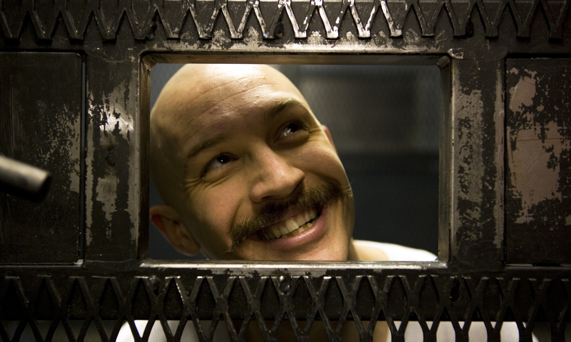 Tom Hardy lächelt durch die Luke einer Gefängnistür. U.a. dank seiner einmaligen Performance ist Bronson bei unseren besten Gefängnisfilmen auf dem Podest gelandet