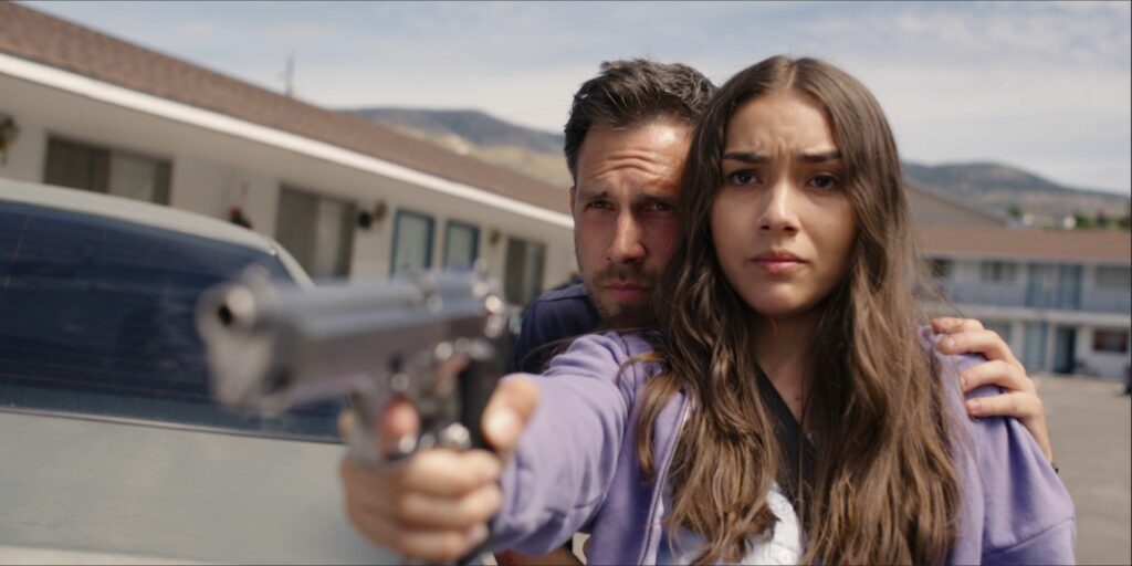 Vor einem Motel richtet Mia die Waffe auf ihre Verfolger, der Dieb stützt sie von hinten und hilft ihr beim Zielen - Bullet Proof