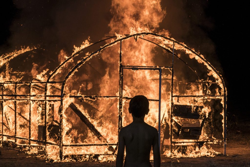 Ein Junge steht vor einem brennenden Gewächshaus in Burning.