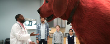 Ein riesiger, roter Hund im Bildvordergrund, dahinter ein Erwachsener, ein Junge und ein Mädchen