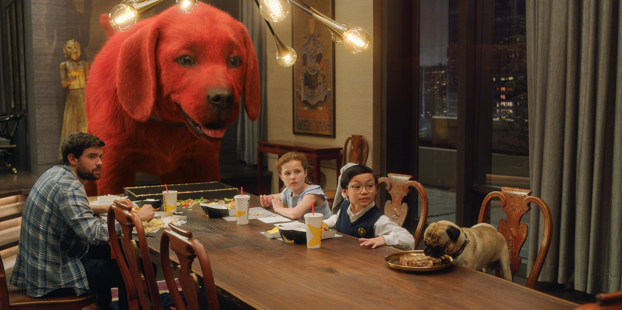 Ein großer roter Hund, rechts daneben zwei Kinder, ein Mädchen und ein Junge, am Essenstisch