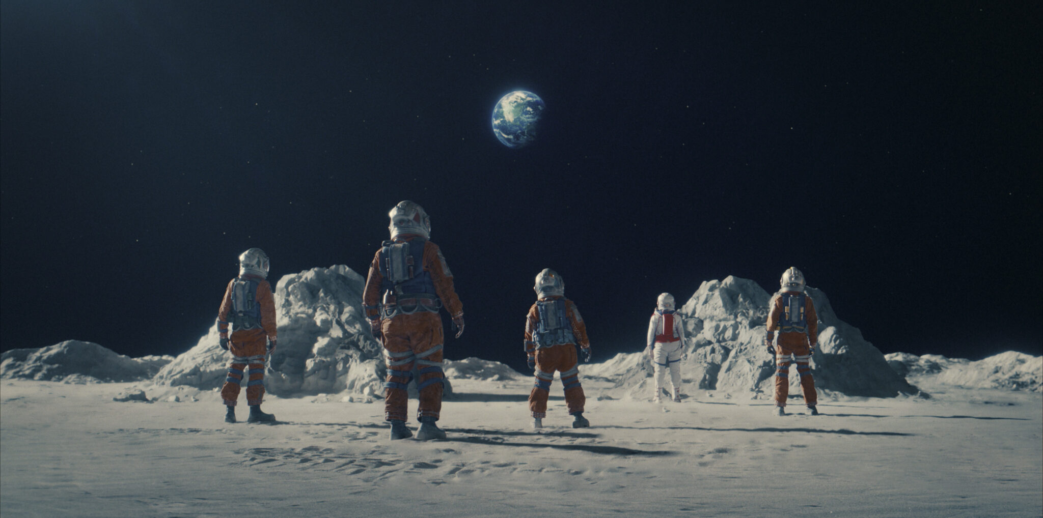 Ein Bild auf der Mondoberfläche mit 5 Astronauten in orangen Outfits. Crater