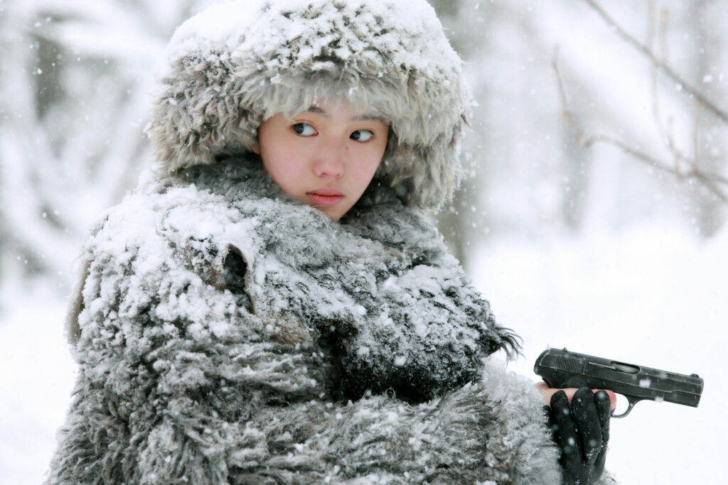 Liu Haocun steht in dicker Pelzkleidung im Schnee und hälte eine Pistole in der Hand - Cliff Walkers