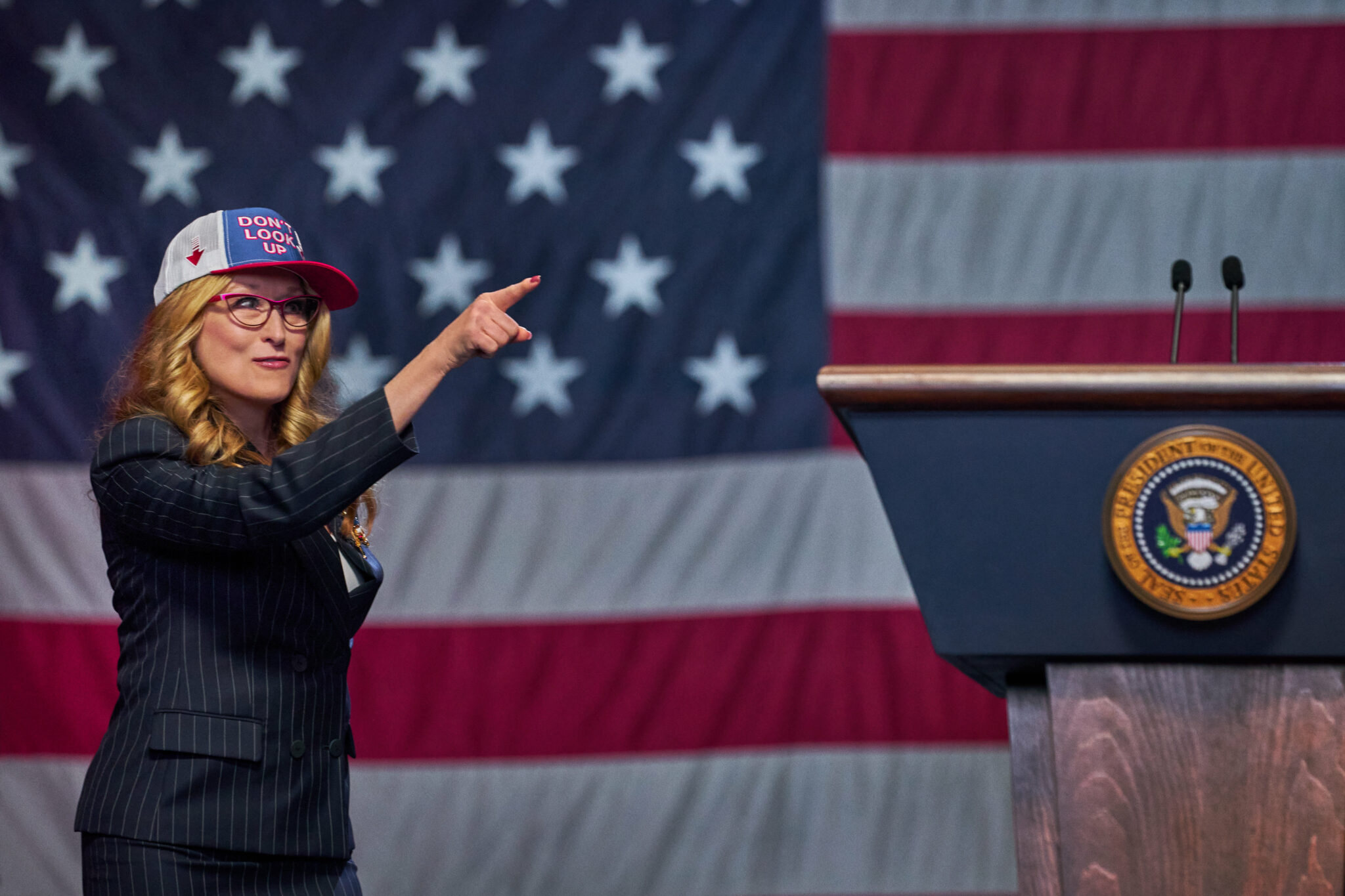 Eine Frau mit einer PR-Cap, neben ihr ein Rednerpult, im Hintergrund die US-Flagge