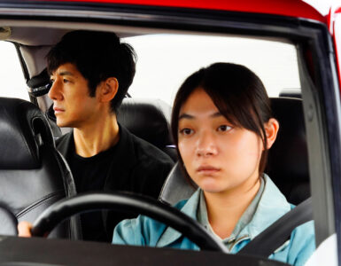 Misaki (Toko Miura) sitzt am Steuer des roten Saabs 900, während Yusuke (Hidetoshi Nishijima) hinter ihr auf der Rückbank sitzt und seitlich aus dem rechten Fenster blickt. Beide wirken angestrengt und erschöpft. Zudem ist die Umgebung außerhalb des Autos nicht erkennbar.