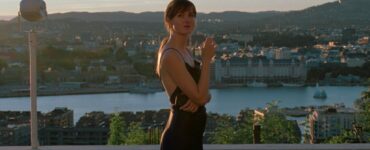 Auf dem Bild sieht man Julie, wie sie auf einem Balkon auf den Sonnenuntergang in Oslo blicken kann und dabei traurig in die Ferne blickt - The Worst Person in the World