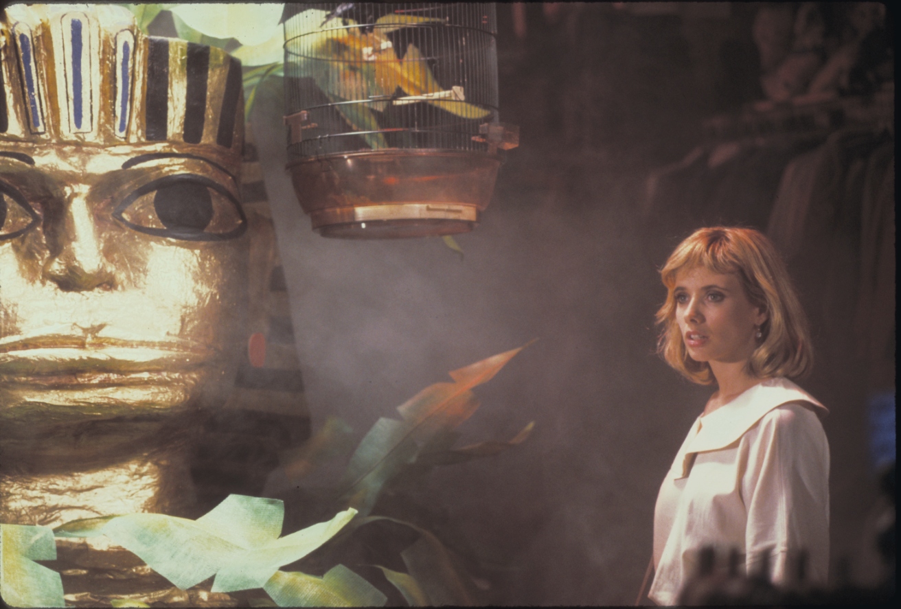 Rosanna Arquette als Roberta steht vor einer Plakatwand zu einer ägyptischen Ausstellung mit einem über ihr hängenden Vogelkäfig in Susan... Verzweifelt Gesucht.