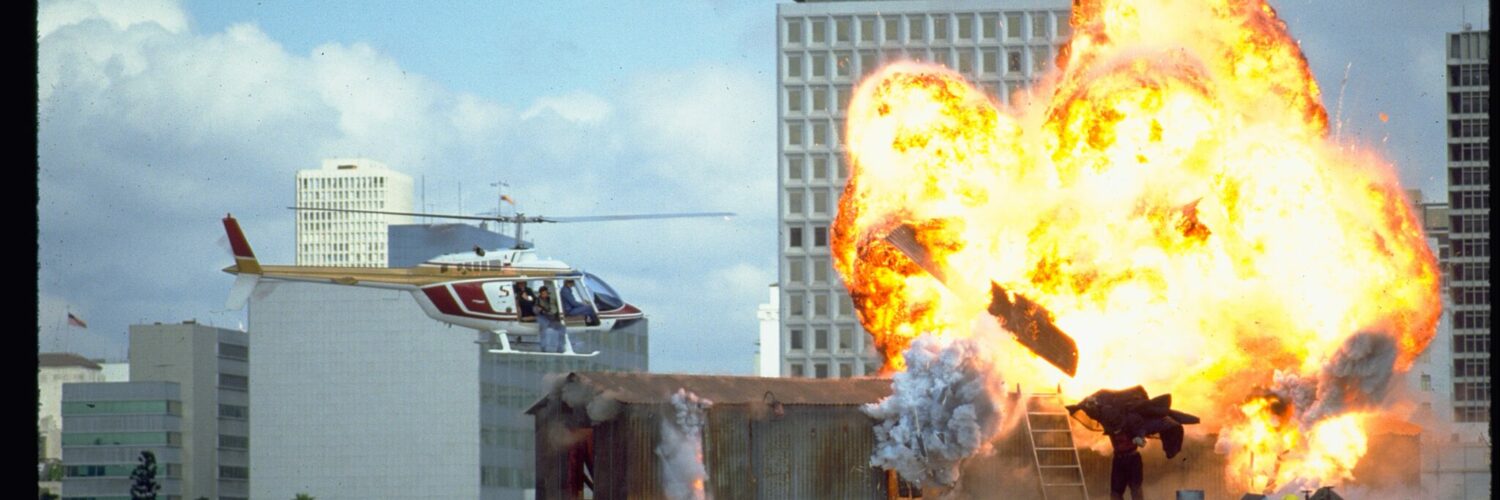 Auf dem Bild sieht man Darkman auf dem Dach eines Hochhauses, wo vor ihm eine Explosion hochgeht und er gleichzeitig von einem Helikopter verfolgt wird - Darkman