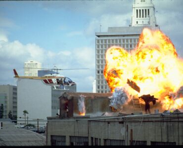 Auf dem Bild sieht man Darkman auf dem Dach eines Hochhauses, wo vor ihm eine Explosion hochgeht und er gleichzeitig von einem Helikopter verfolgt wird - Darkman