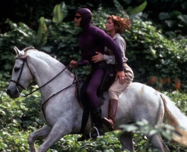 Billy Zane alias Das Phantom reitet auf einem weißen Pferd, hinter ihm sitzt Kristy Swanson in einem beigefarbenen Abenteureroutfit und schulterlangen rotbraunen Haaren. Im Hintergrund ist der Dschungel zu sehen.