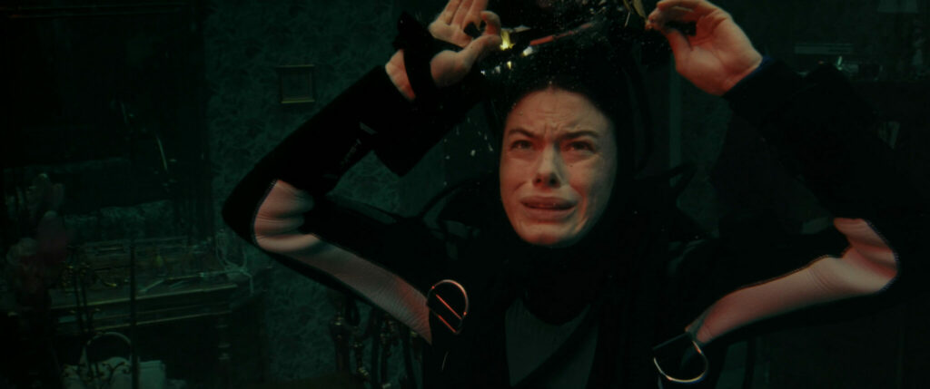 Im Film The Deep House hat sich Camille Rowe als Tina bei einem Tauchgang ihre Atemmaske vom Gesicht gerissen, hält ihre Luft an und schaut verunsichert in das dunkle Wasser um sie herum