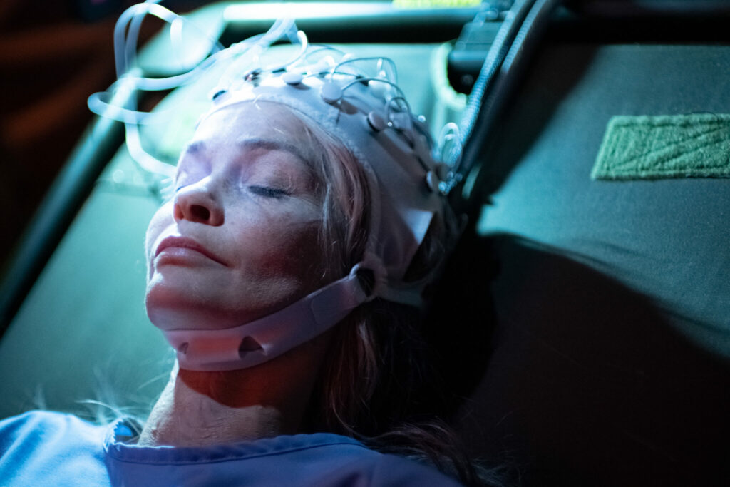 Nathalie Boltt als Angela liegt im Film Demonic auf einer Liege und hat eine technologische Haube auf den Kopf geschnallt