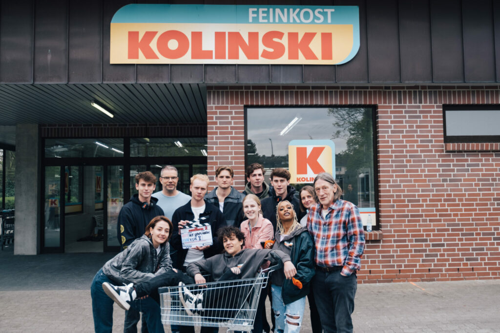 Das Produktionsteam von Die Discounter hat sich vor der Drehlocation, dem Supermarkt Feinkost Kolinski aufgestellt