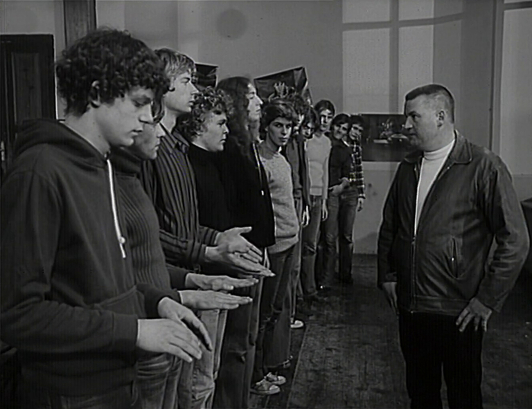 Schwuchow steht rechts im Bild und schaut die Gruppe Jugendlicher an. Diese stehen in einer Reihe und die vordersten drei strecken ihre Hände hervor.