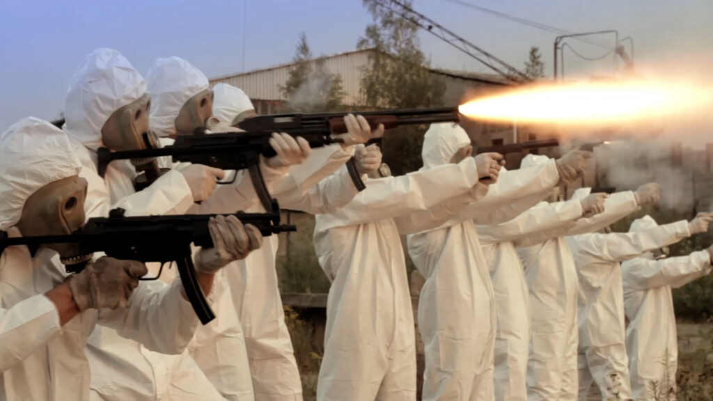 Eine Reihe in weiße Schutzanzüge und Gasmasken gekleidete Männer feuert mit schweren Geschützen - Atomic Eden.
